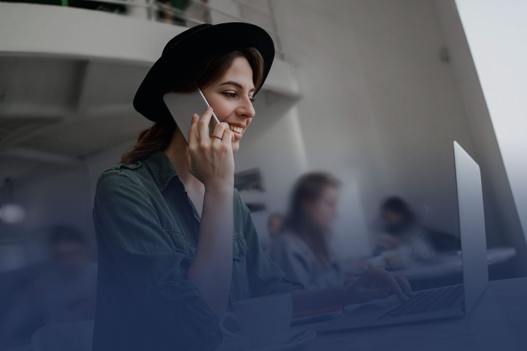 A young woman talks on a mobile phone, while sitting at a table on her laptop, working remotely. But is she working securely?